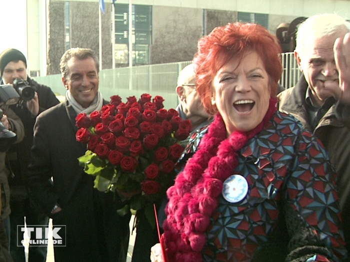 Regina Ziegler und Michel Friedman haben einen Strauß rote Rosen für Kanzlerin Angela Merkel dabei
