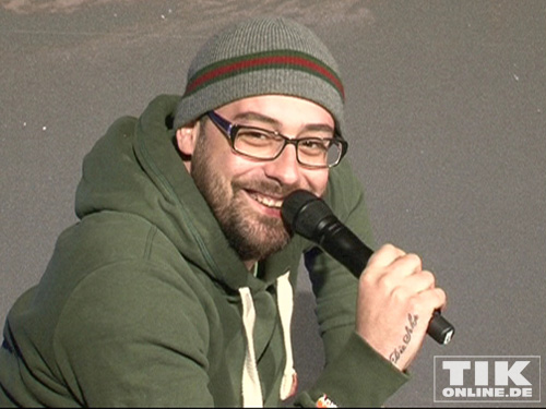 Sido in grünem Kapuzenpulli und Wollmütze mit Brille und Bart. An der